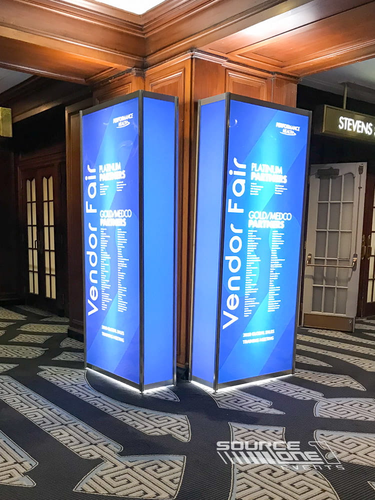 Purple illuminated backlit tower display highlighting conference branding with modern lighting and premium event graphics.
