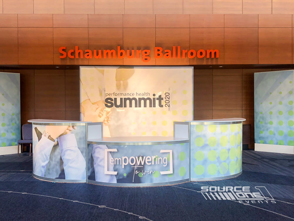 Warm-toned registration entrance with orange conference branding and directional signage leading attendees into event spaces.