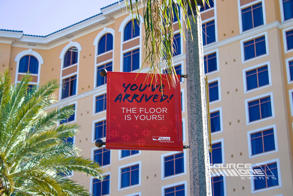 Multiple blue hanging banners suspended throughout a convention center providing branding and directional wayfinding for attendees.