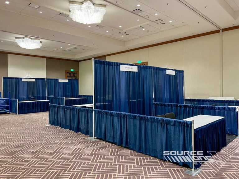 Blue pipe-and-drape exhibit booths with registration counters and modular event setup inside a convention center.