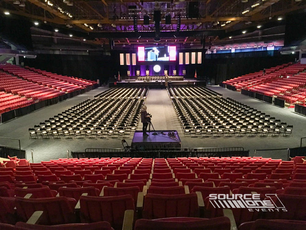 Expansive keynote stage with red seating, large projection screens, professional stage lighting, and center presentation platform inside a convention center ballroom.