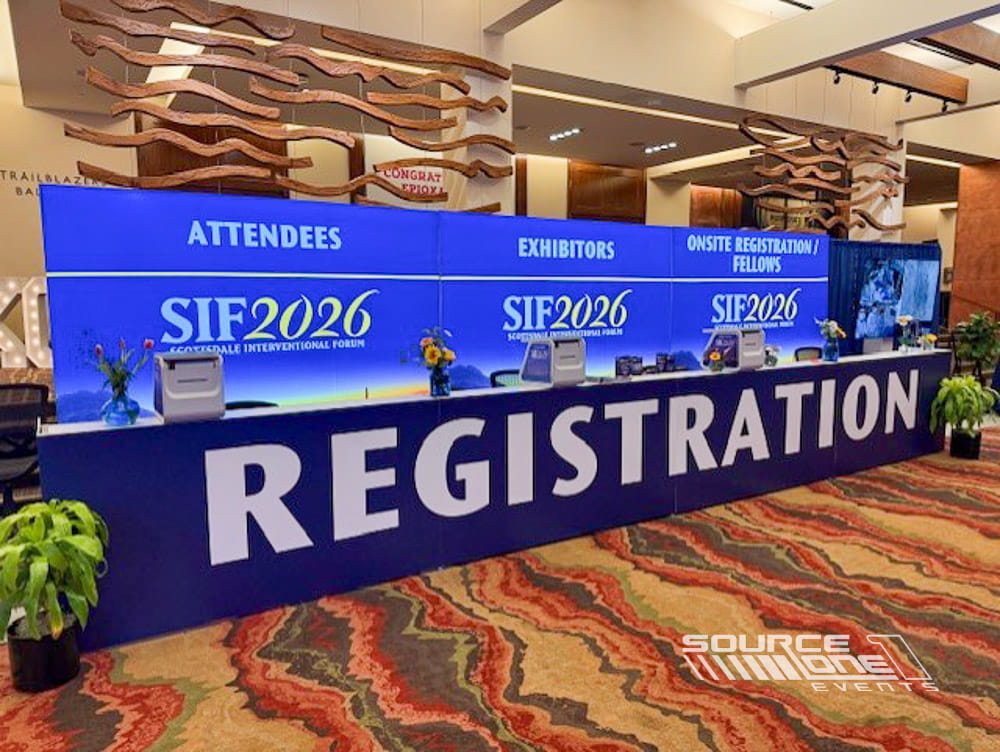 Large branded registration counter with bold blue graphics and attendee service stations for conference check-in.