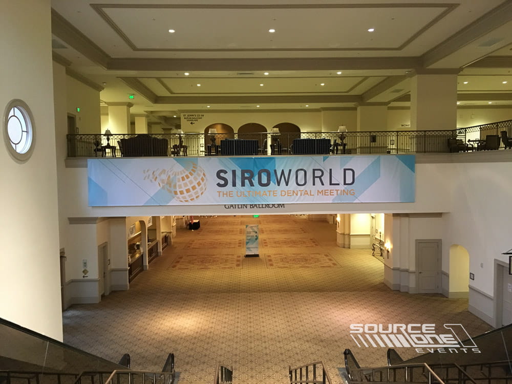 Large overhead conference banner installed across a ballroom entrance featuring branded event graphics and directional messaging.