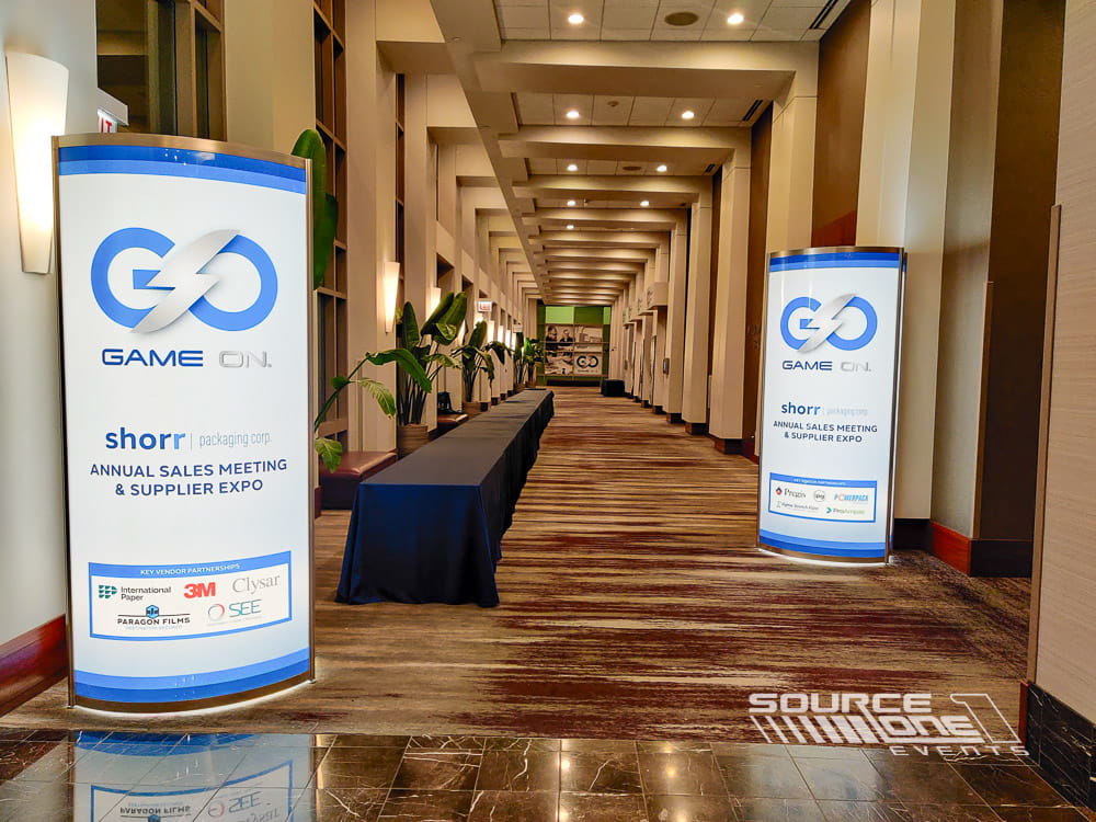 Blue illuminated entrance columns with branded graphics creating a welcoming registration experience for conference attendees.