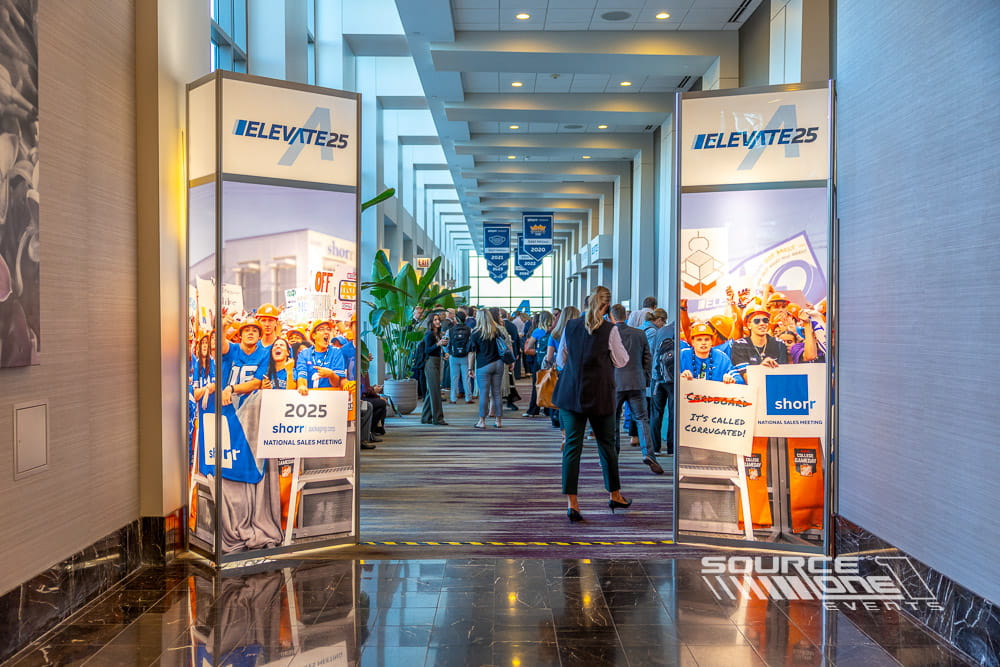 Tall illuminated entrance towers featuring blue branded graphics welcoming attendees into the conference registration area.