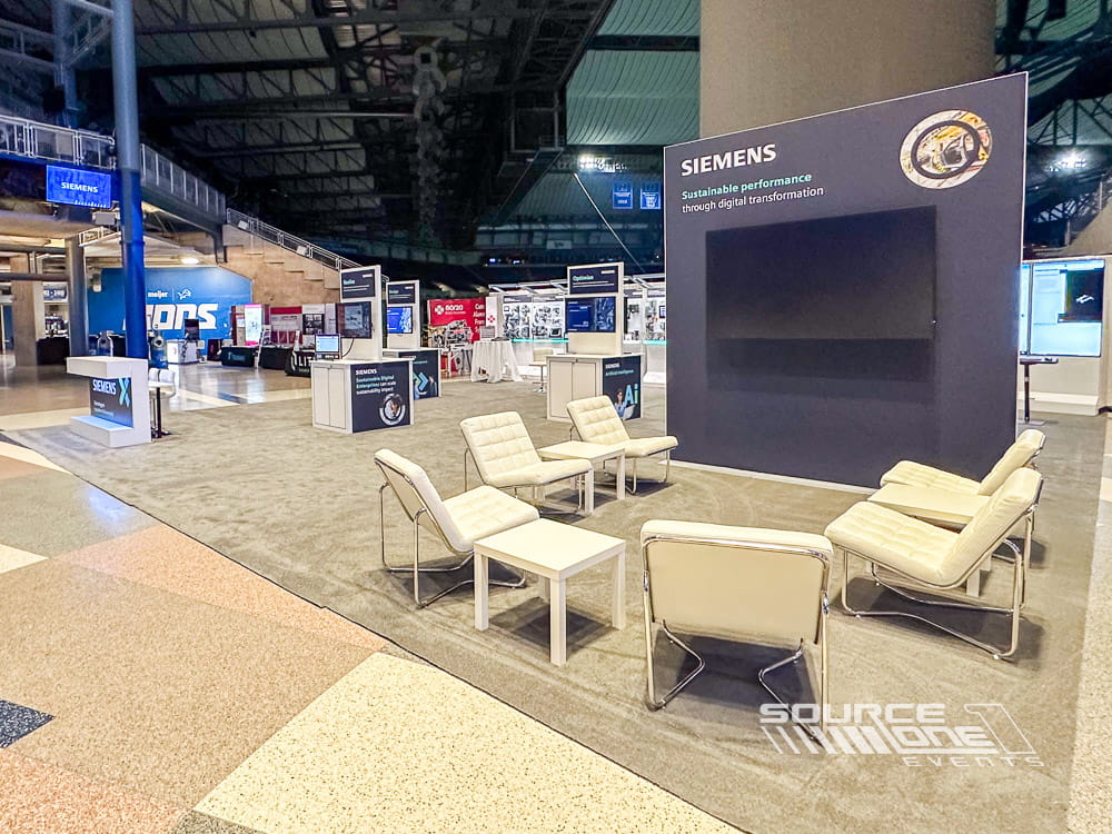 Open custom exhibit with product displays, digital media, and collaborative meeting areas inside the trade show floor.