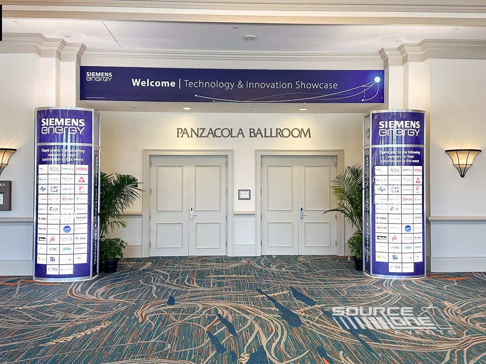Blue and white backlit tower displays framing conference registration with bold corporate branding and integrated lighting.