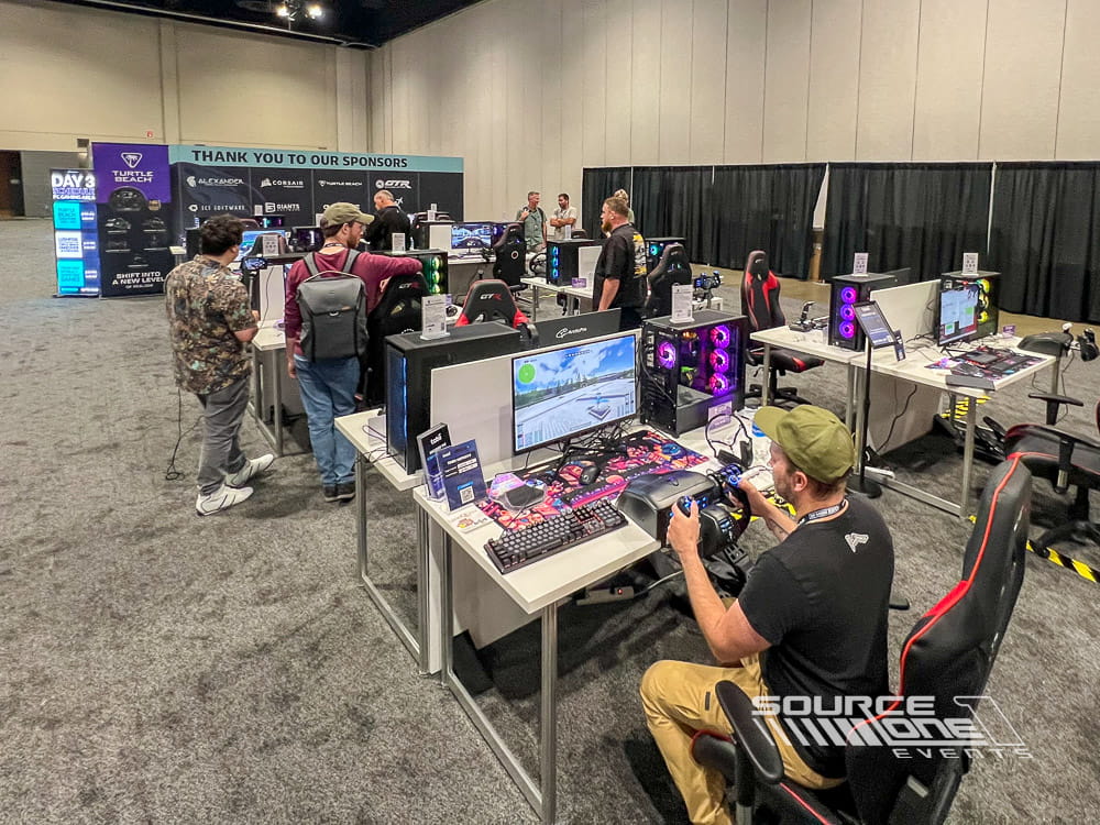 Interactive gaming area with gaming stations, attendees, and tournament equipment inside the trade show floor.