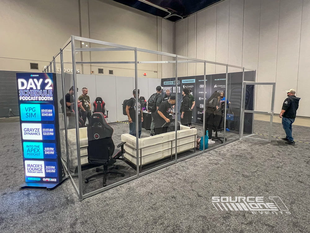 Glass-enclosed podcast recording booth providing a professional sound-isolated space for live interviews and content creation during a trade show.
