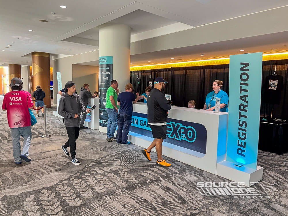 Registration entrance with suspended branded signage, attendee check-in counters, and colorful exhibit hall graphics.