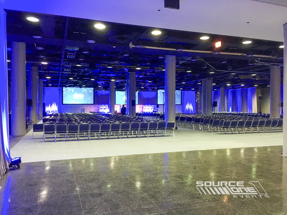 Large conference general session stage with blue lighting, presentation screens, and audience seating.
