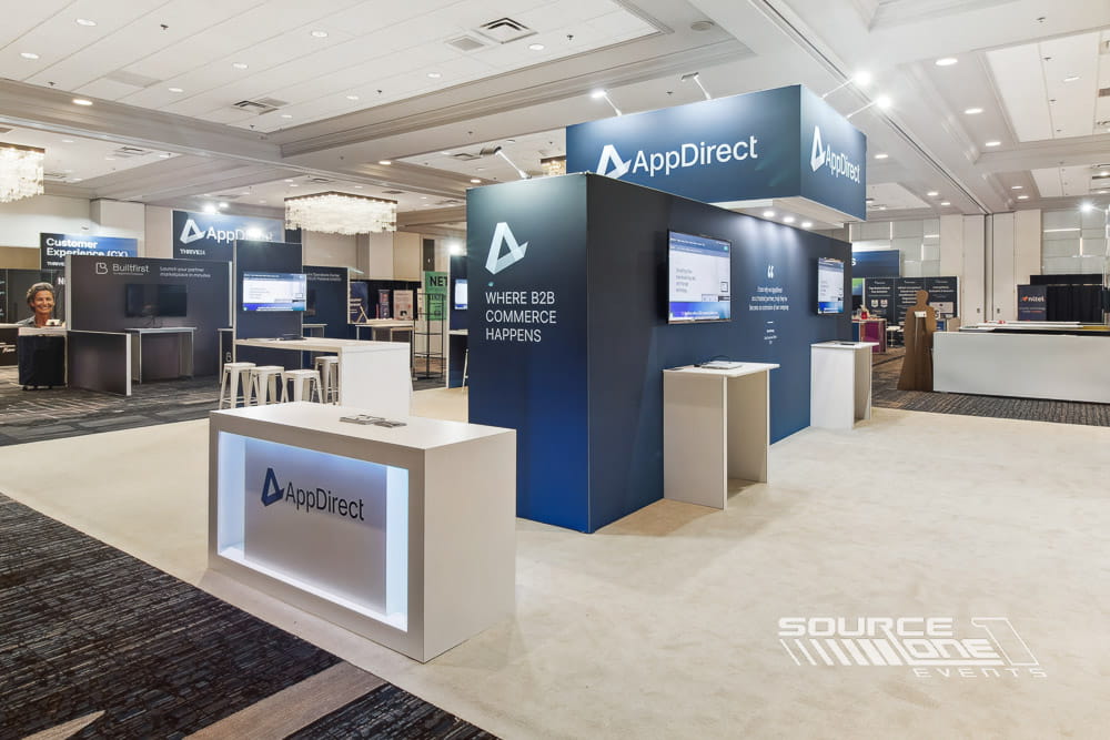 Spacious exhibit environment with branded architecture, reception counters, meeting tables, and digital presentations.