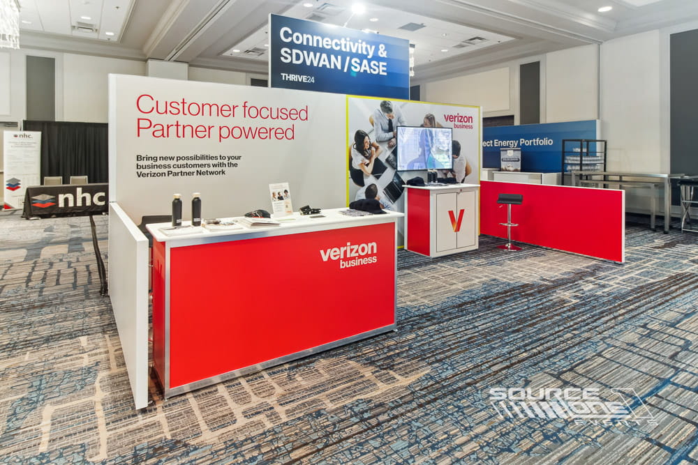 Red and white branded exhibit booth featuring reception counter, digital displays, and custom architectural finishes.