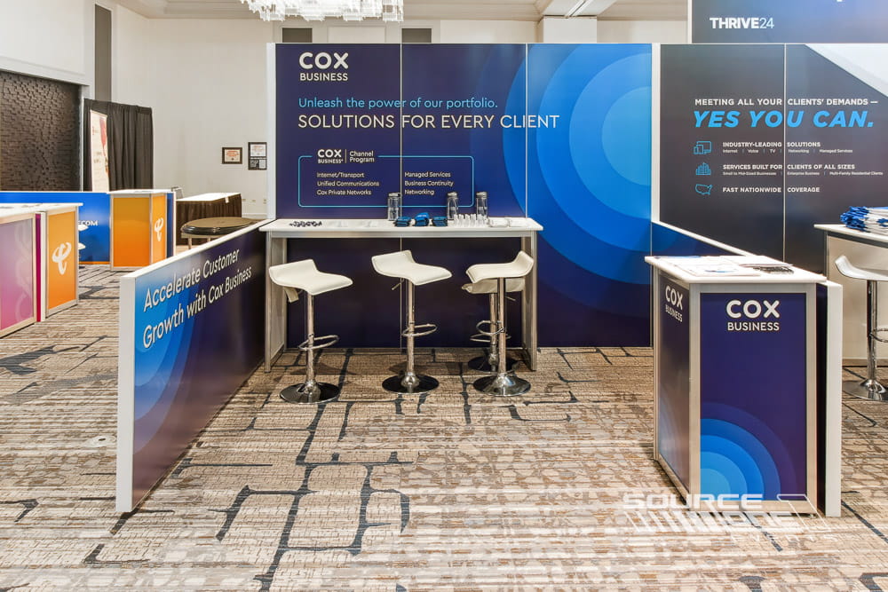 Corporate exhibit featuring blue gradient graphics, reception counter, digital monitor, and custom hardwall construction.