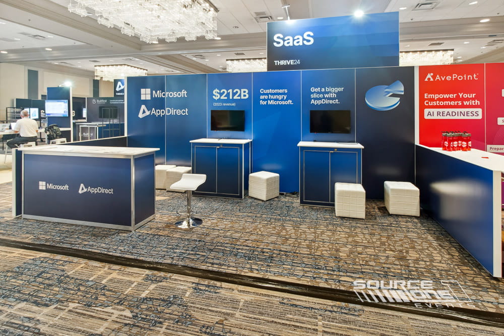 Modern custom hardwall booth featuring overhead branded signage, digital displays, and open meeting areas for attendee interaction.