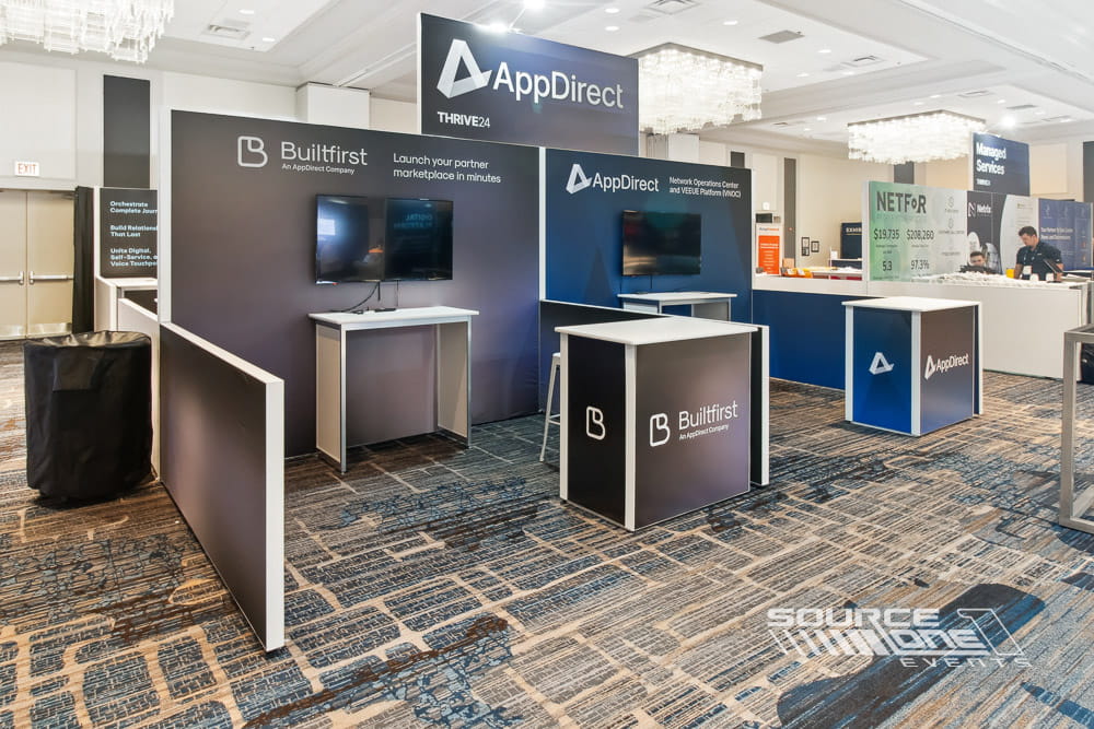 Premium custom exhibit featuring AppDirect branding, LED displays, reception counters, and contemporary architecture.