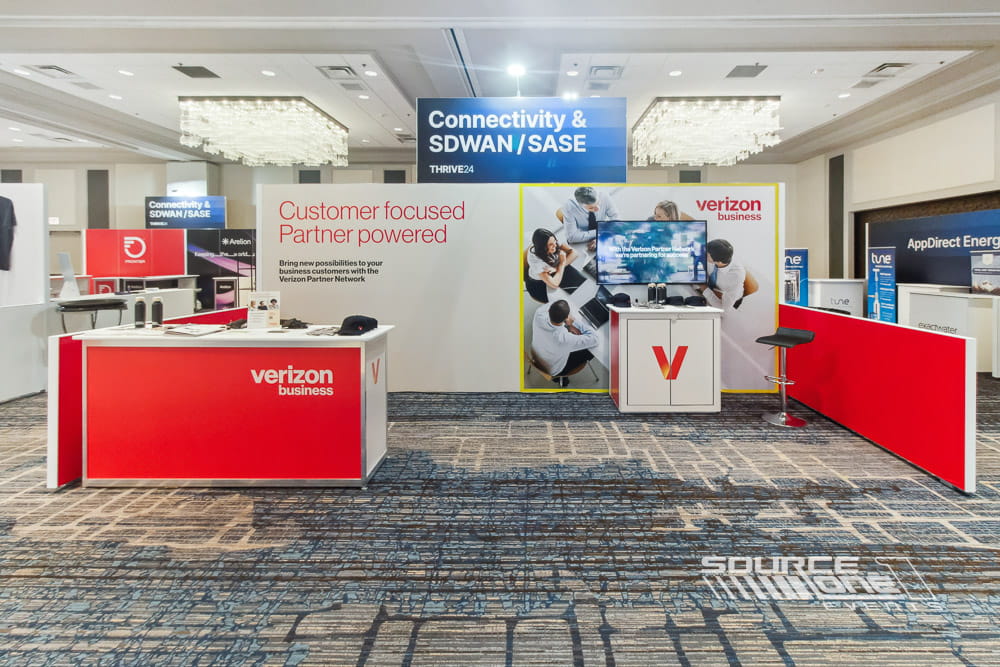 Large hardwall exhibit booth with blue corporate branding, custom counters, integrated monitors, and premium architectural construction.