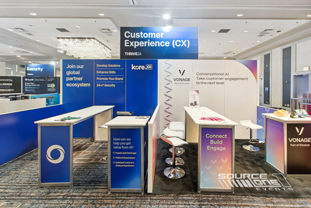 Custom exhibit featuring white reception counters, blue branded walls, and digital presentation screens for attendee engagement.
