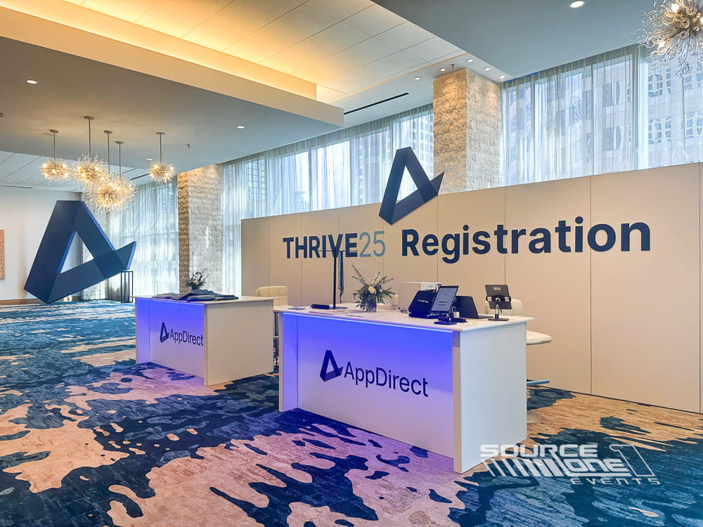 Contemporary registration area featuring blue branded counters, digital displays, and attendee check-in stations designed by Source One Events.