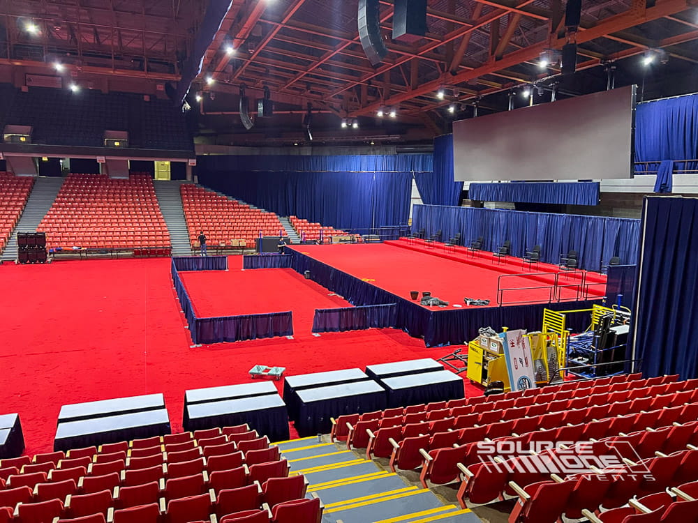 Large commencement stage featuring red carpeting, audience seating, and professional event production.