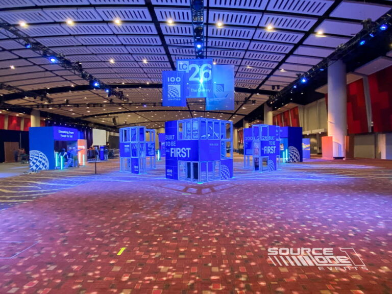 Large suspended cube signs with illuminated United Airlines branding hanging above the trade show floor for wayfinding and brand visibility.