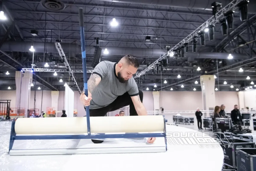 Event worker assembling exhibit flooring inside a convention center.