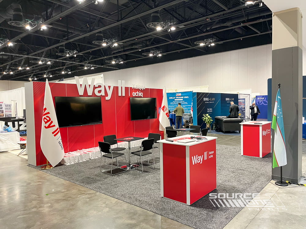 Modern custom trade show booth featuring bold red graphics, product displays, meeting space, and interactive attendee engagement areas.
