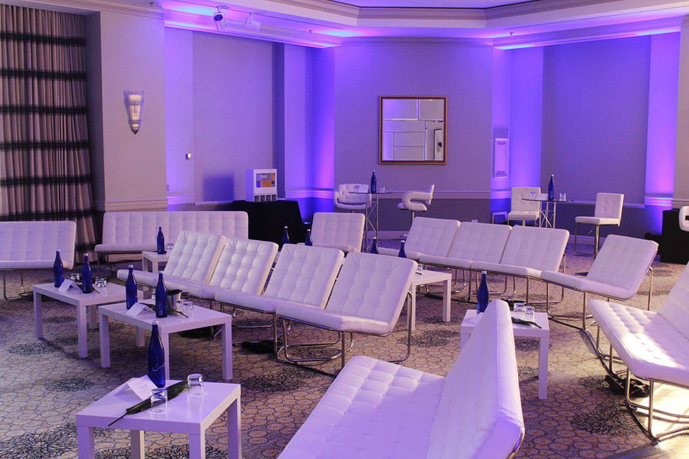 Elegant event lounge with white sofas and purple uplighting for corporate reception