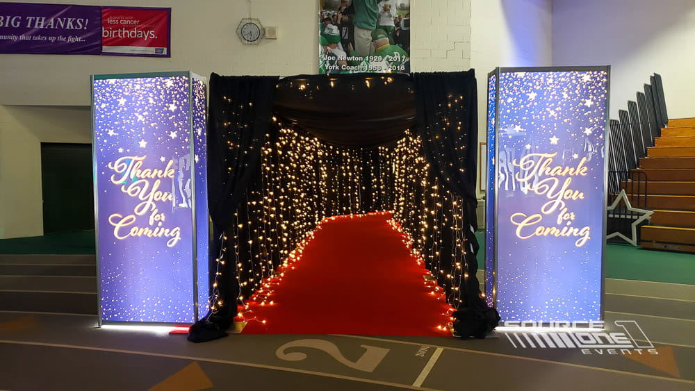 Elegant black backlit tower display featuring illuminated event branding and decorative lighting for a formal gala entrance.