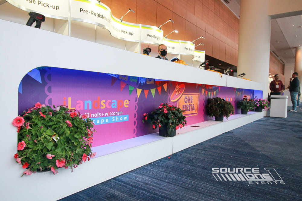 Bright registration desk featuring colorful landscape-themed branding, attendee service counters, and convention center lobby graphics.